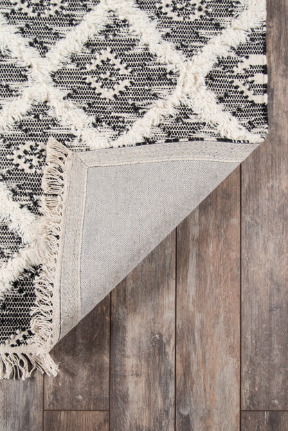 Woven black and ivory geometric rug with fringed edges, folded to show beige backing on wood floor.