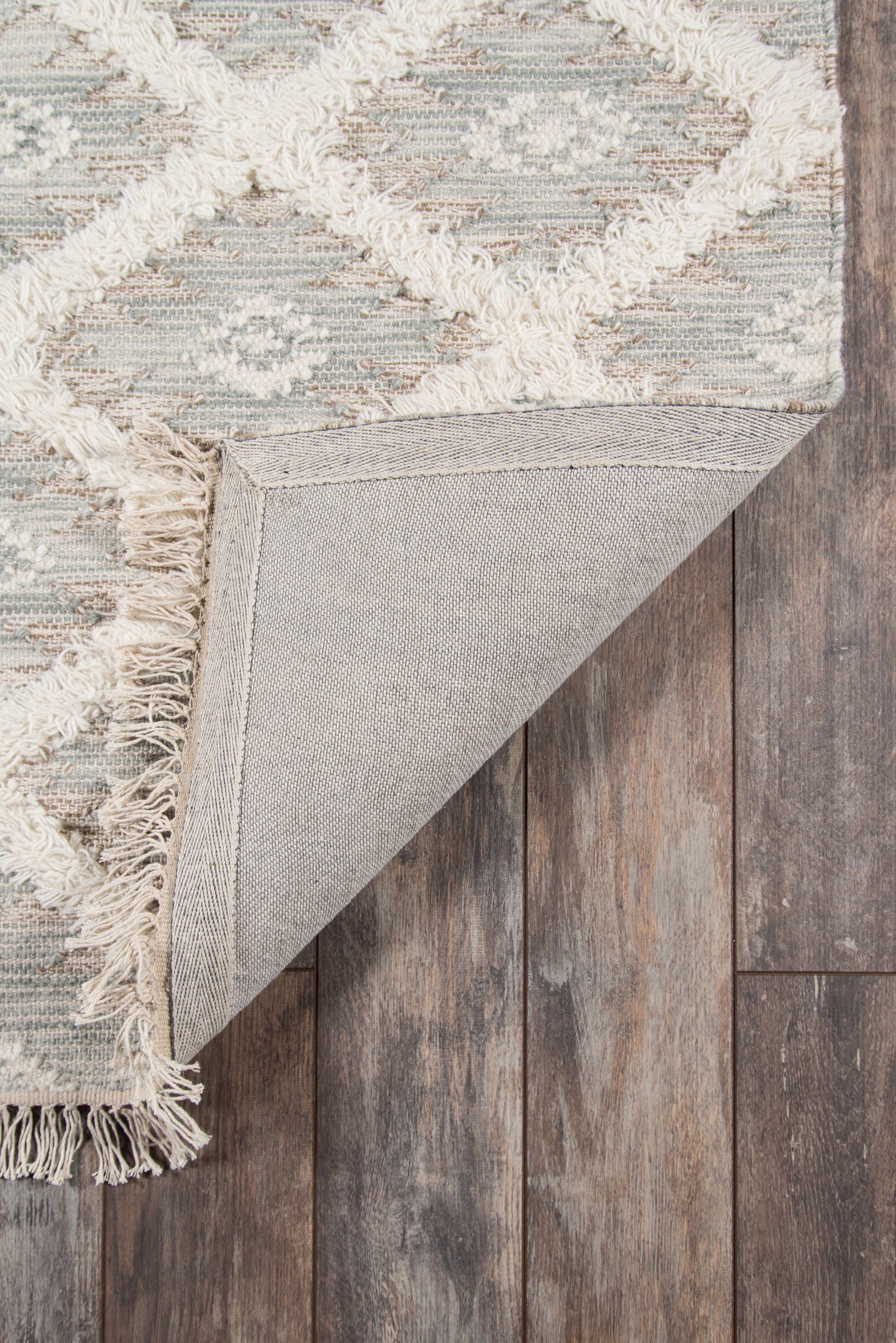 Grey geometric area rug with ivory fringe, turned corner shows underside on rustic wood floor.