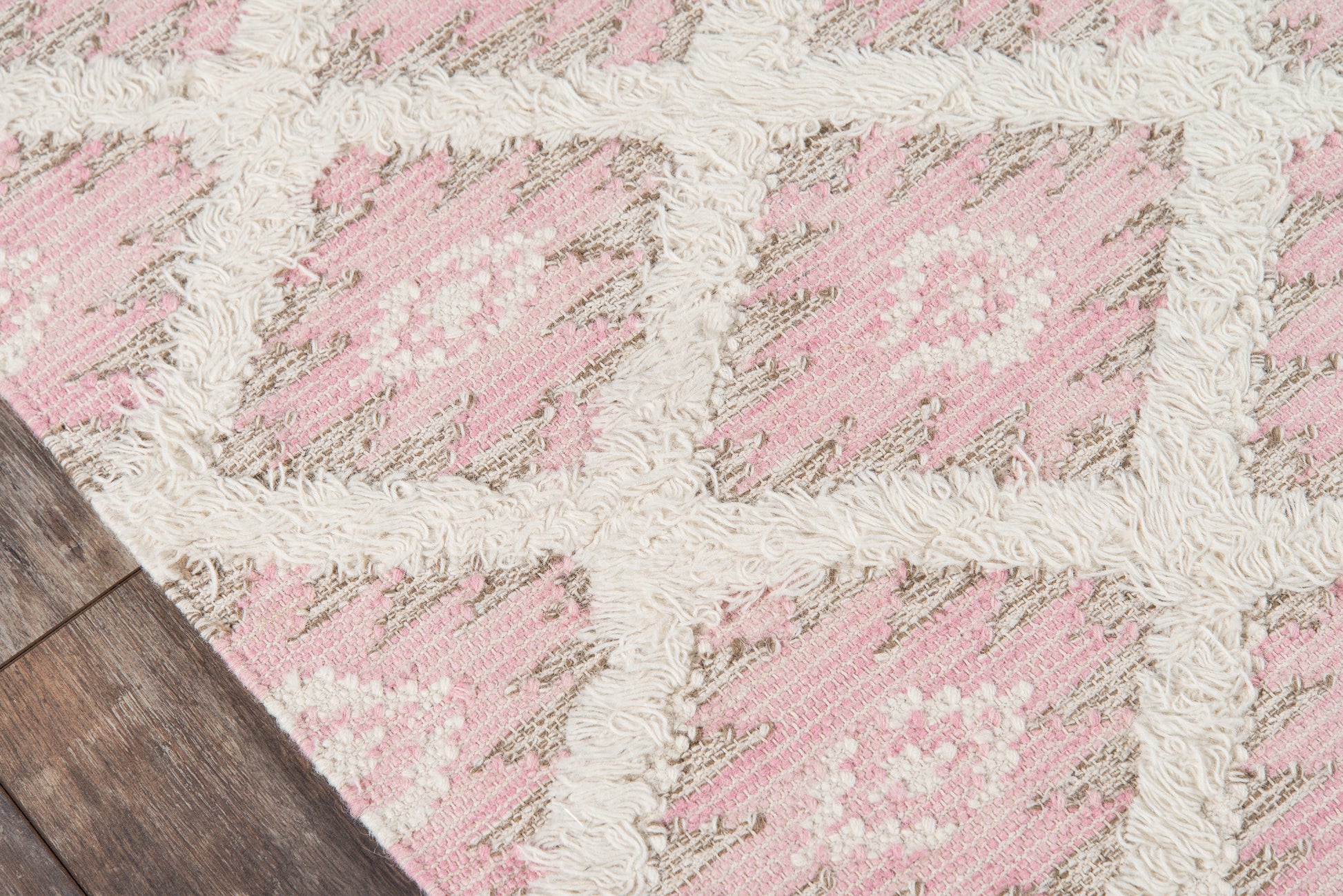 Pink and cream geometric shag rug on dark wood floor, plush pile with ivory fringe, modern boho style.