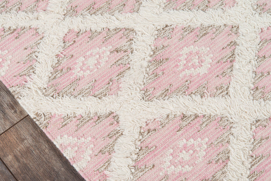 Pink and ivory geometric shag rug with cream fringe on wood floor.