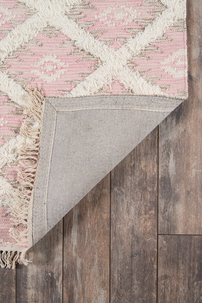 Pink geometric rug with ivory tassels and woven motif; folded corner reveals grey backing on wood floor.