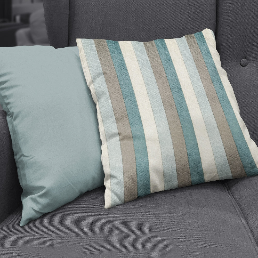 Two throw pillows on a dark gray sofa; one solid teal, the other blue, beige and gray striped.