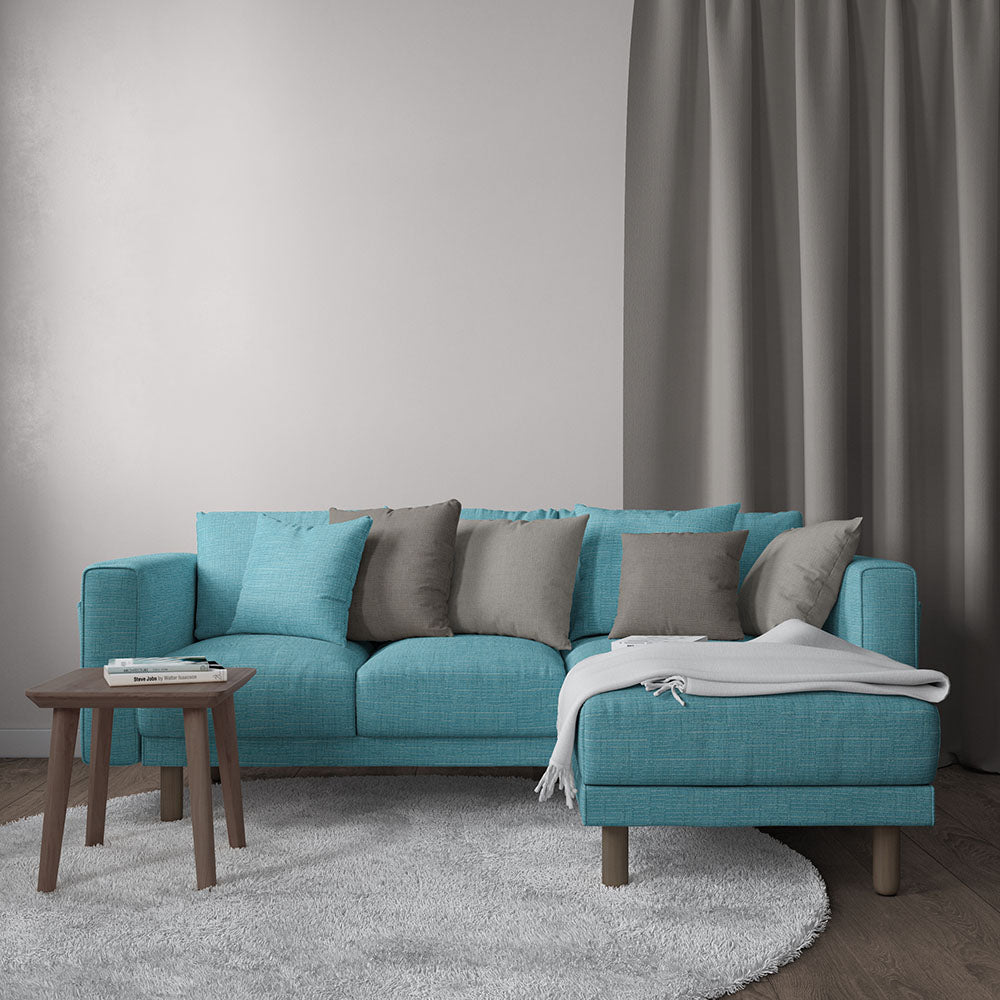 Teal fabric sectional sofa with chaise, grey and teal cushions, light throw, wooden legs in a modern living room.
