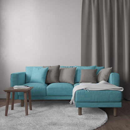 Teal fabric sectional sofa with chaise, grey and teal cushions, light throw, wooden legs in a modern living room.