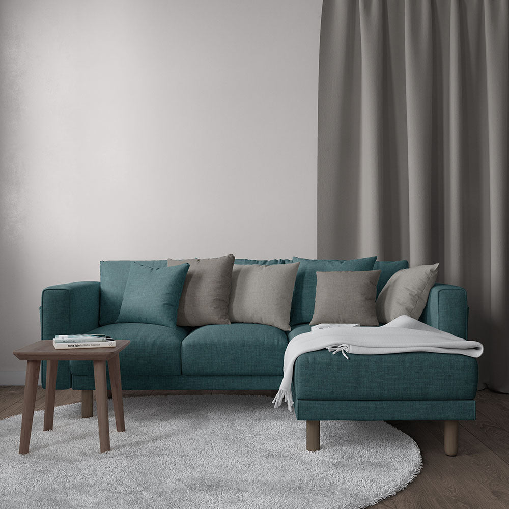 Teal sectional sofa with chaise, beige and gray cushions, white throw blanket, round wooden coffee table, gray rug.