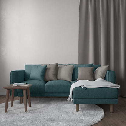 Teal sectional sofa with chaise, beige and gray cushions, white throw blanket, round wooden coffee table, gray rug.