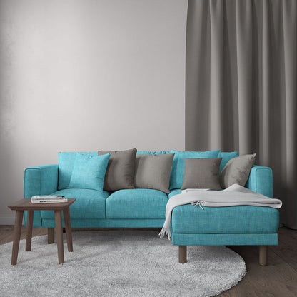 Teal fabric sectional sofa with chaise on right, grey cushions, light throw, wooden coffee table, grey rug and curtains.