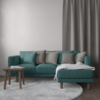 Teal L-shaped sofa with gray and beige cushions, white throw, wooden legs, round gray rug and small wooden coffee table