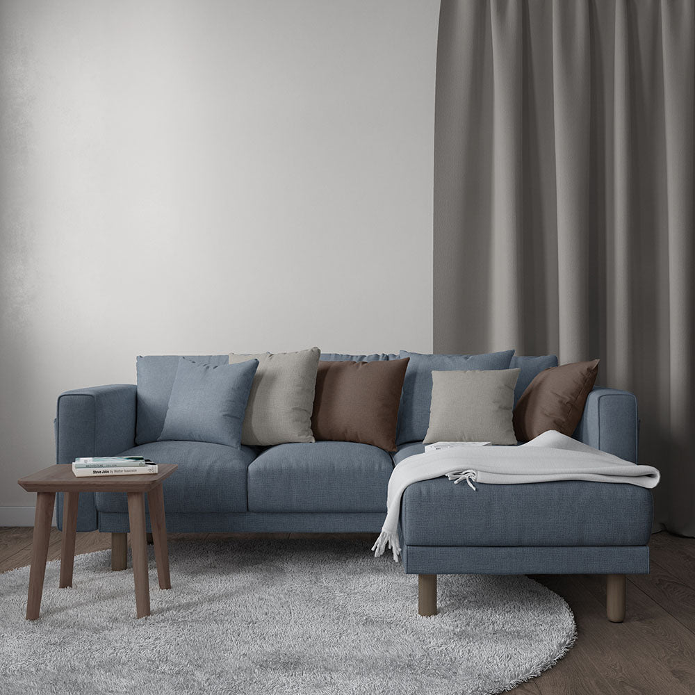 Blue-gray fabric sectional with chaise, multicolor cushions, wooden legs, and gray throw blanket in modern living room.