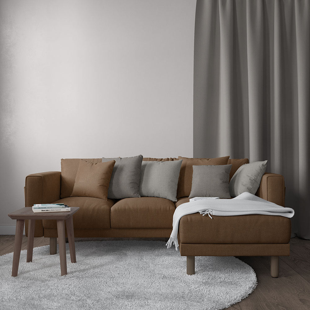 Brown fabric sectional sofa with gray & beige cushions, wooden legs; gray throw blanket, round wood coffee table, grey rug.