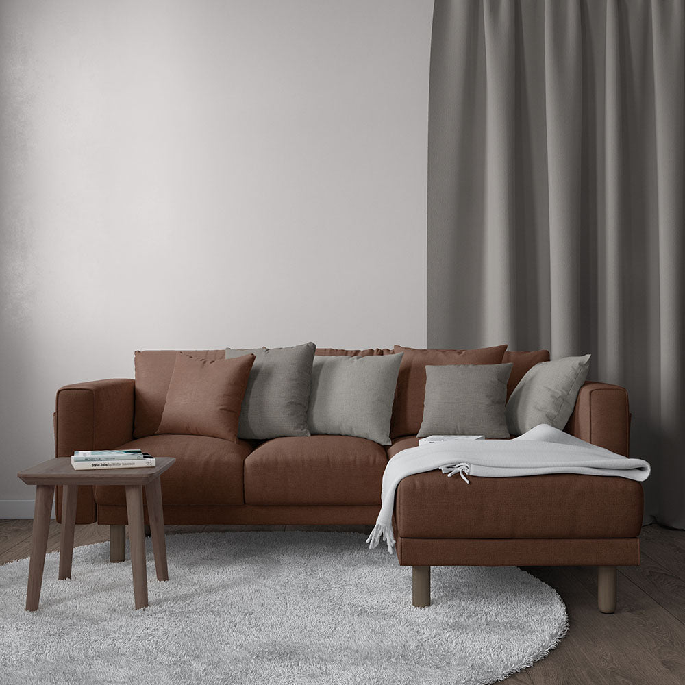 Modern brown L-shaped sectional sofa with chaise, gray & taupe cushions, white throw, round wood coffee table, gray rug.