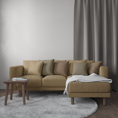 Beige fabric sectional with chaise, white throw blanket, neutral cushions, small wooden side table with magazines, grey rug.