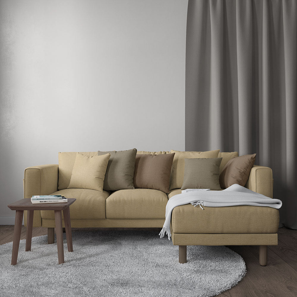 Beige sectional with chaise, neutral cushions, white throw, wooden side table and gray rug.