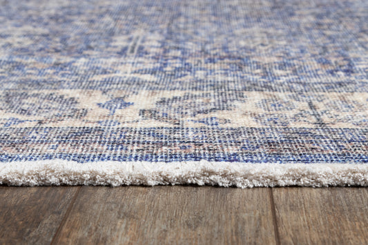 Blue & ivory distressed patterned area rug with white fringe edge on a wooden floor.