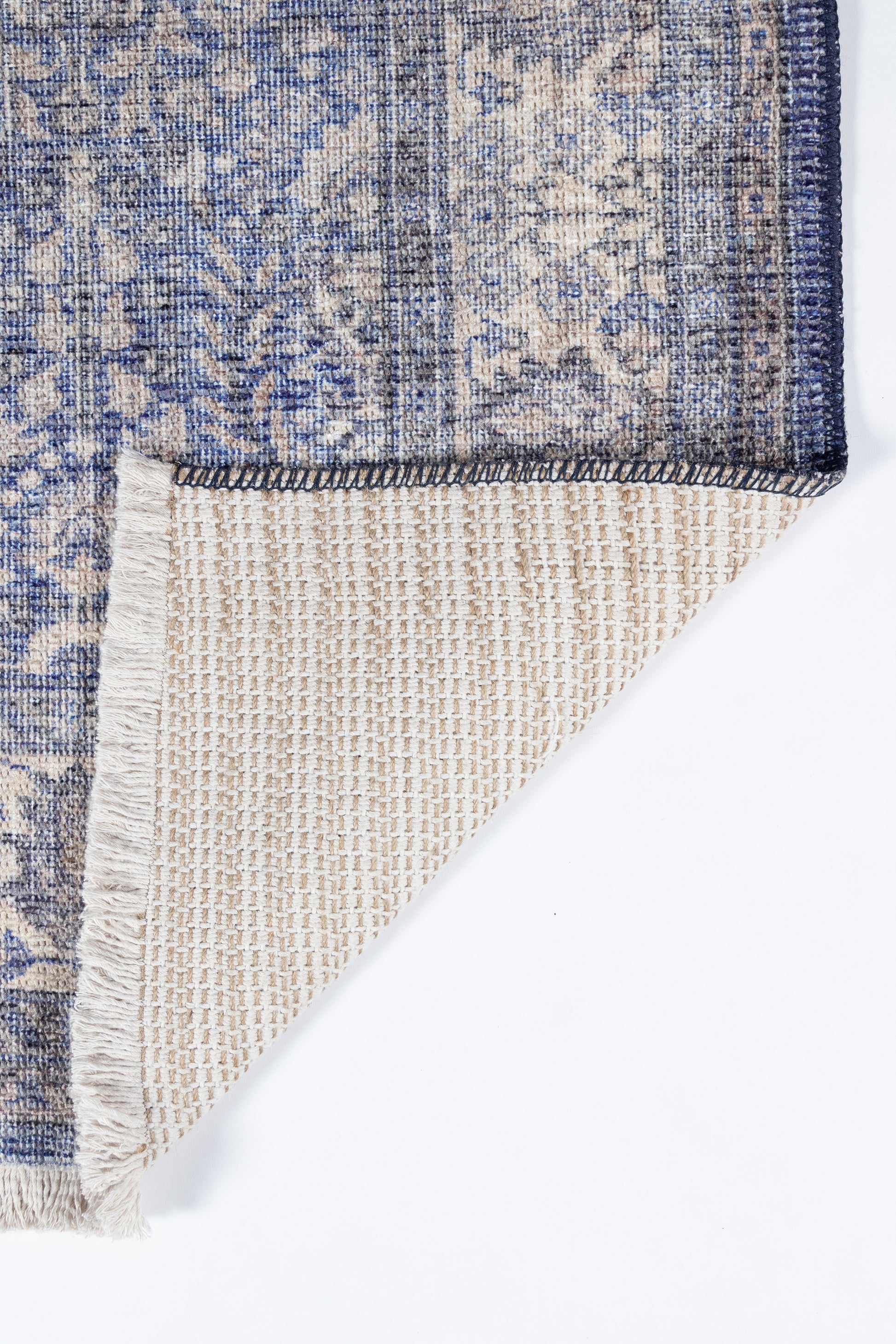 Blue and beige floral patterned rug, folded to reveal its beige woven underside and dark navy border.