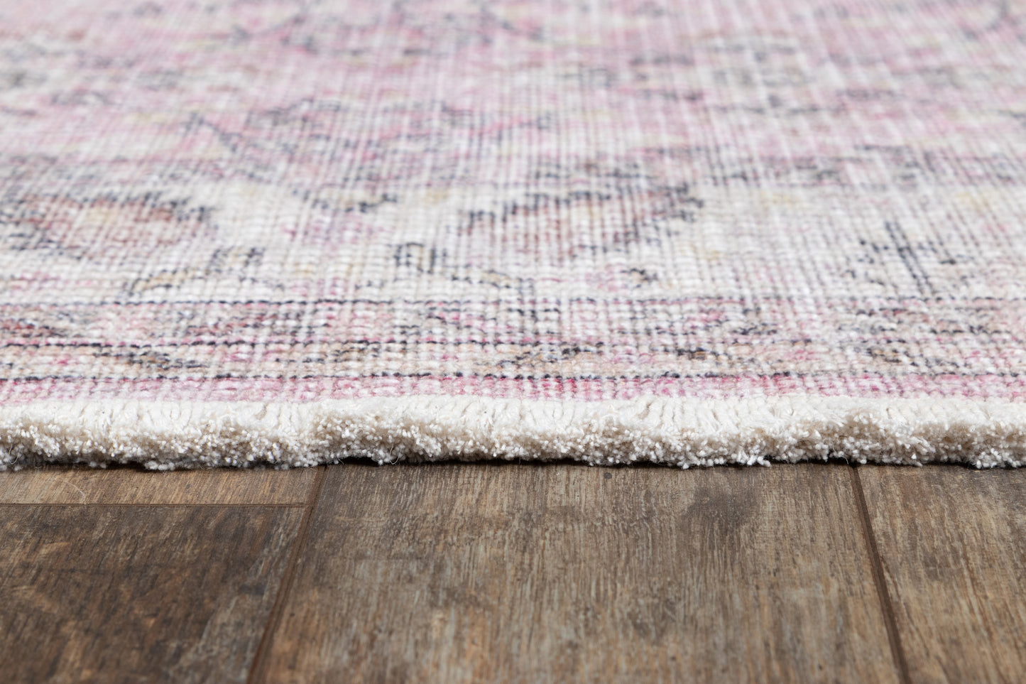 Close-up of a pink and ivory patterned rug with fluffy white fringe resting on wood flooring.