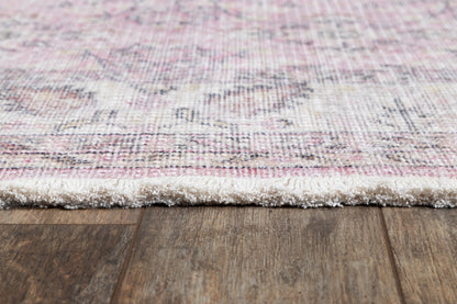 Close-up of a pink and ivory patterned rug with fluffy white fringe resting on wood flooring.