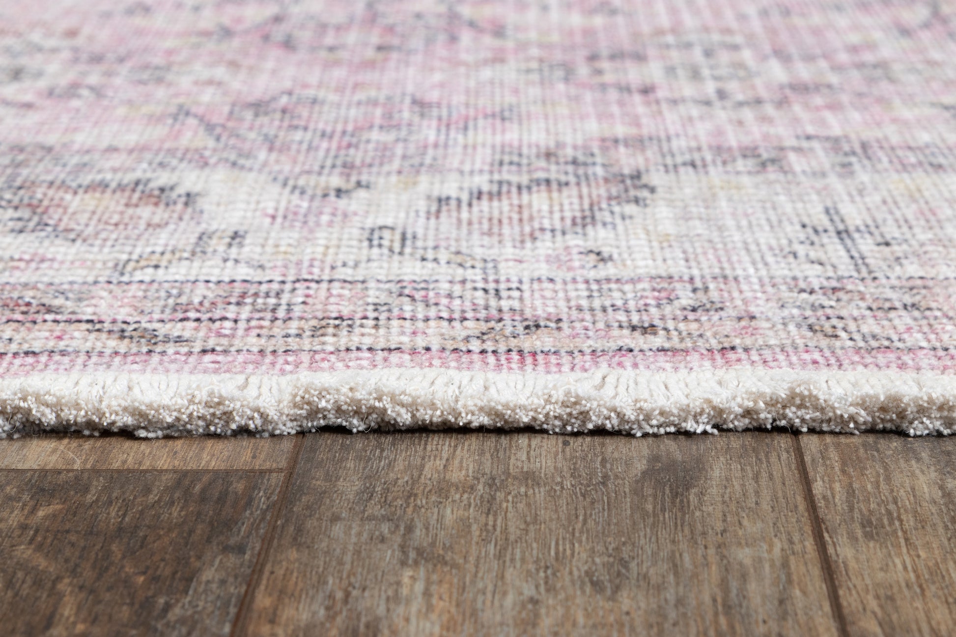 Pink, ivory and gray woven runner rug with fluffy fringe edge on a dark wooden floor.