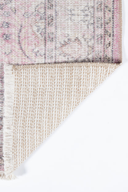 Pink and cream floral rug with fringed edges; folded corner reveals beige woven backing.