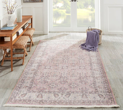 Soft pink Persian-inspired runner rug with a floral border, in a bright living room beside a wicker bench and lavender throw.