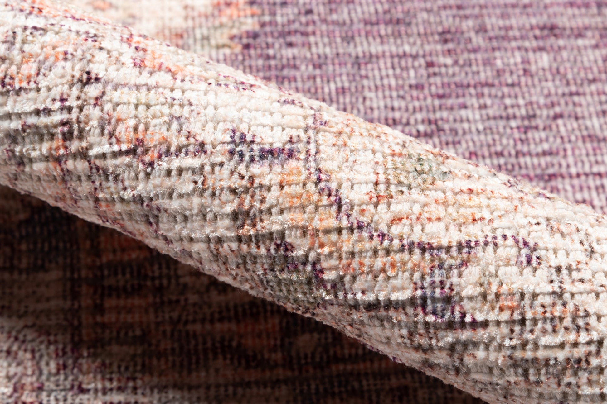 Close-up of a cream textured rug with purple and orange woven pattern and a folded edge.
