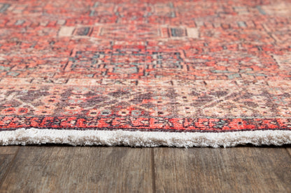 Close-up of a red oriental rug with geometric motifs and white fringe on a wood floor.