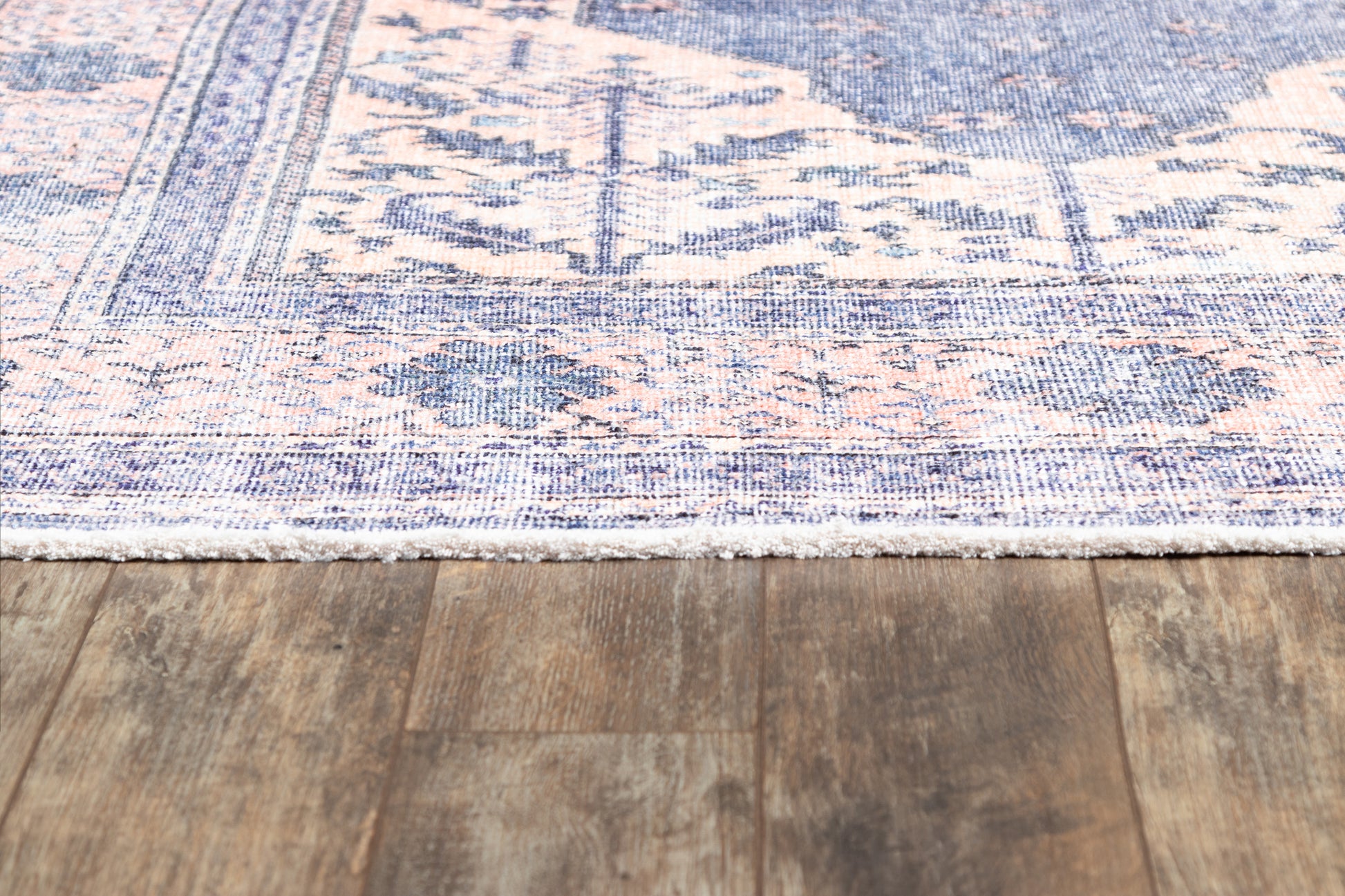 Blue and peach Persian-style area rug with ornate border and white fringe on wood floor.