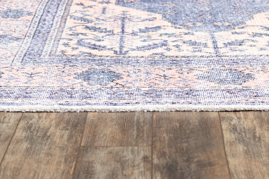 Blue and peach Persian-style area rug with ornate border and white fringe on wood floor.