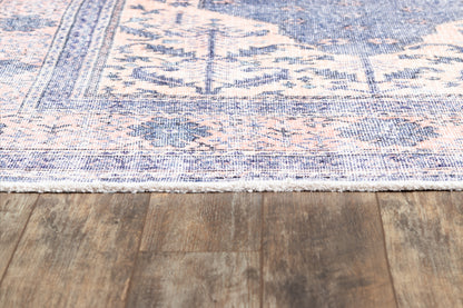 Rectangular woven rug in blue and peach tones with a floral medallion pattern and white fringe on a wood floor.