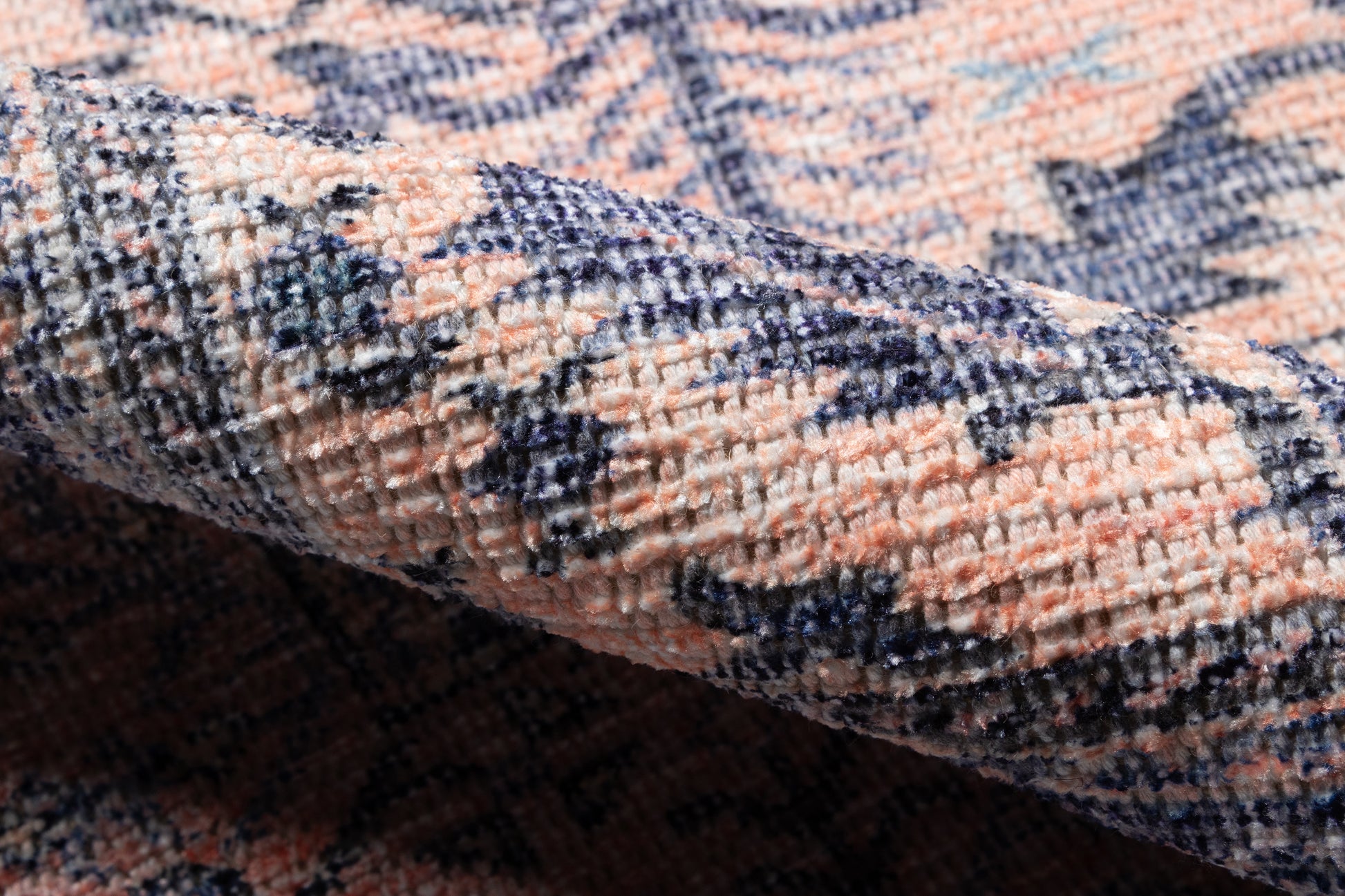Close-up of a plush woven rug with peach, navy blue and cream patterns, folded to show soft pile and texture.