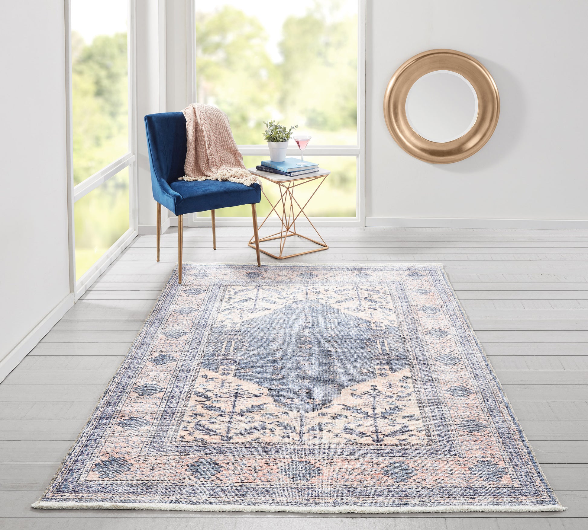 Blue-pink rug, 5' x 8', in a sunlit corner with a blue velvet chair, blush throw, copper geometric side table, and round gold mirror.