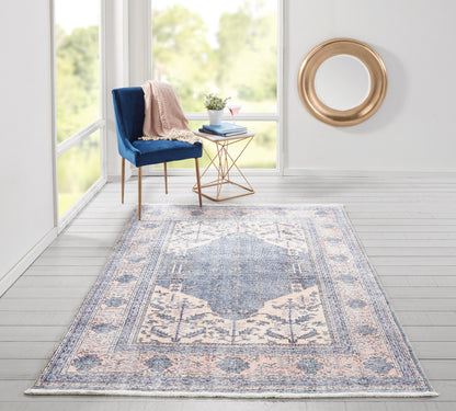 Blue patterned runner rug on floor; blue velvet chair with blush throw, copper geometric side table, plant, pink cocktail; round gold mirror.