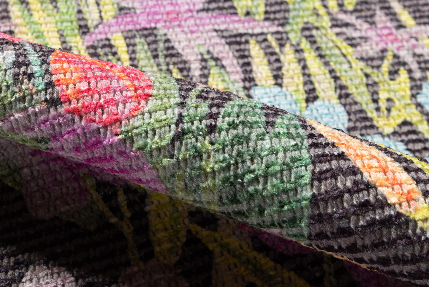 Colorful textured woven rug with vibrant greens, pinks, yellows and purples; folded corner shows thick pile.