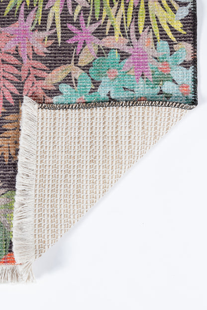 Vibrant tropical floral rug with dark background, pinks, greens and yellows; folded corner reveals beige woven underside.