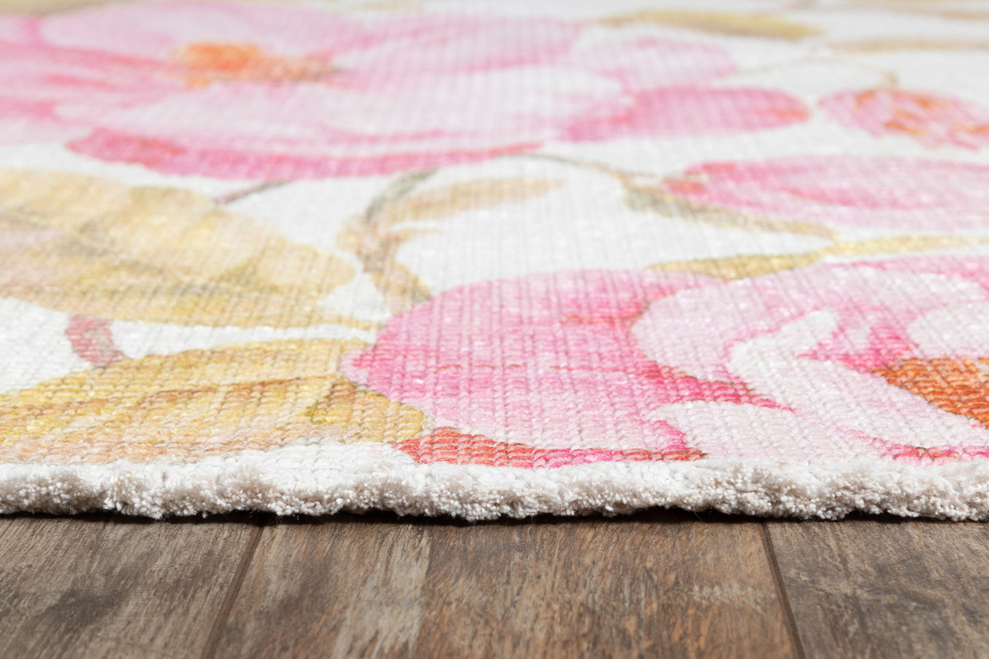 Soft cut-pile floral area rug in pinks, yellows and coral on white, shown on a wooden floor.