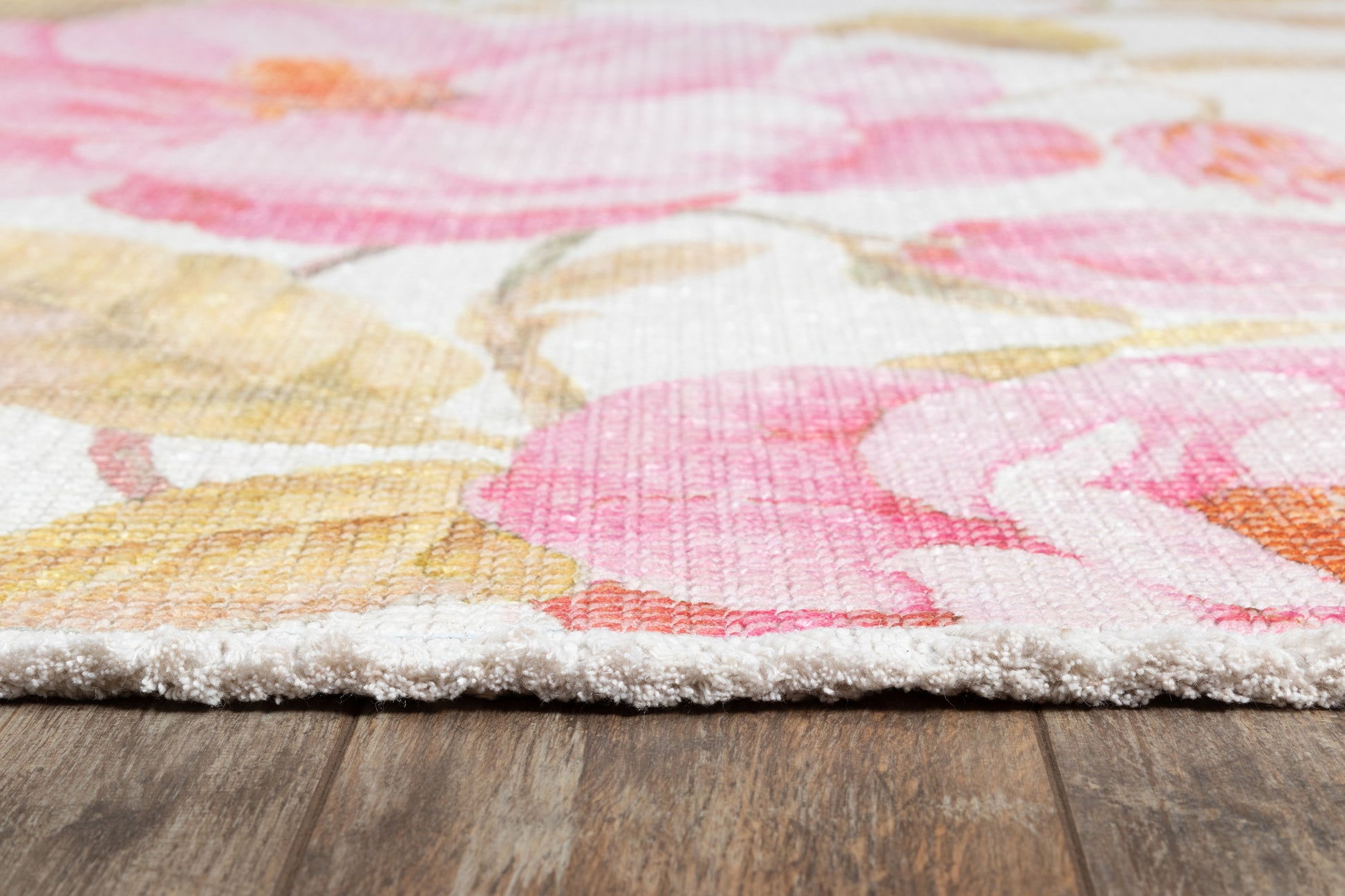 Soft cut-pile floral area rug in pinks, yellows and coral on white, shown on a wooden floor.