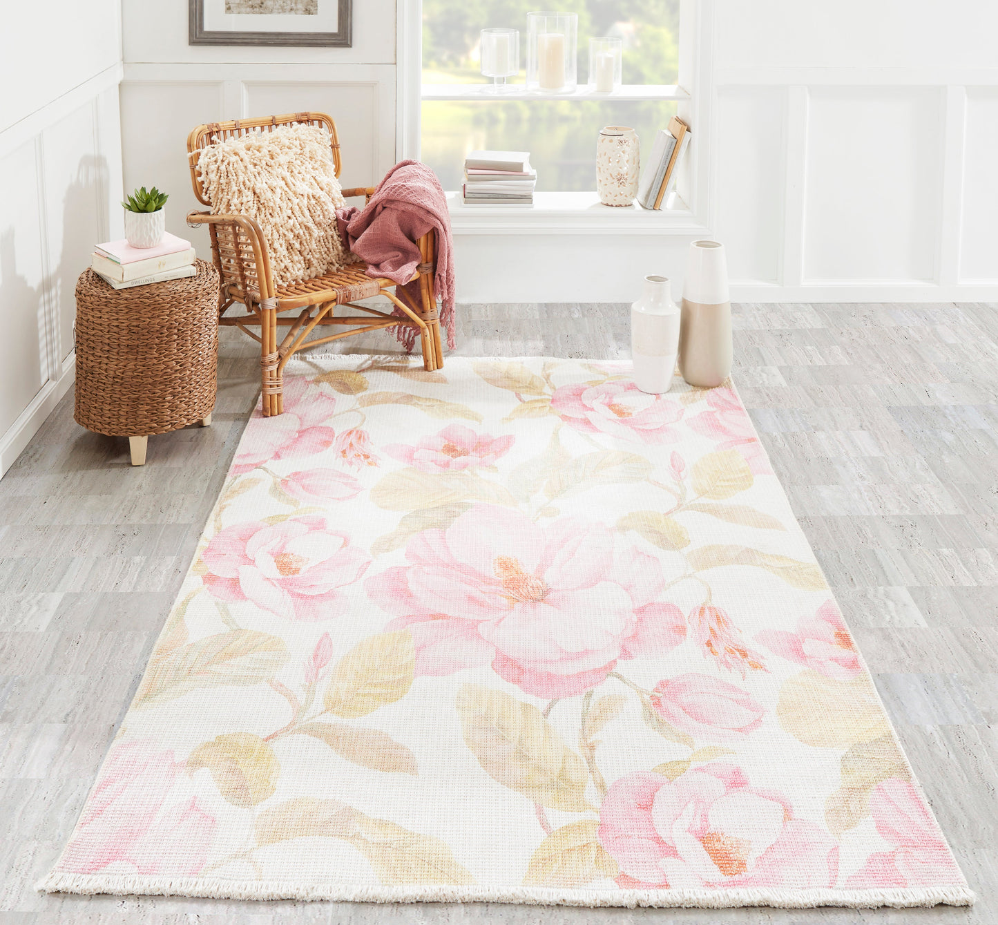 Floral pink peony area rug on light background, in a bright room with wicker chair, pink throw, and woven side table.
