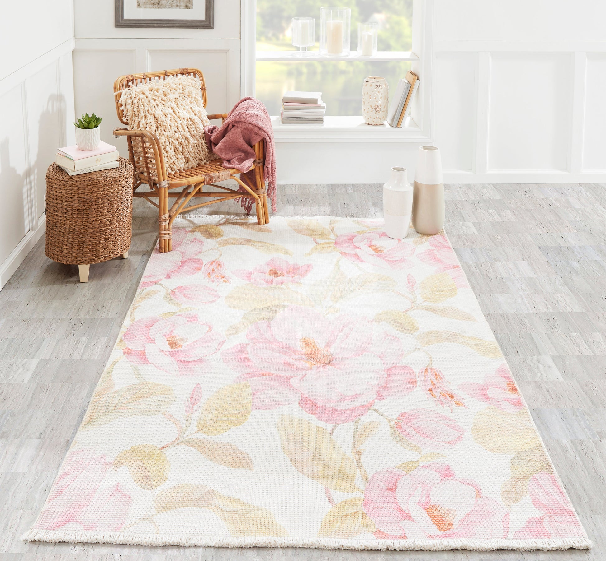 Woven floral runner rug in soft pinks & creams, laid in a bright room with wicker chair, pink throw, & decorative vases.