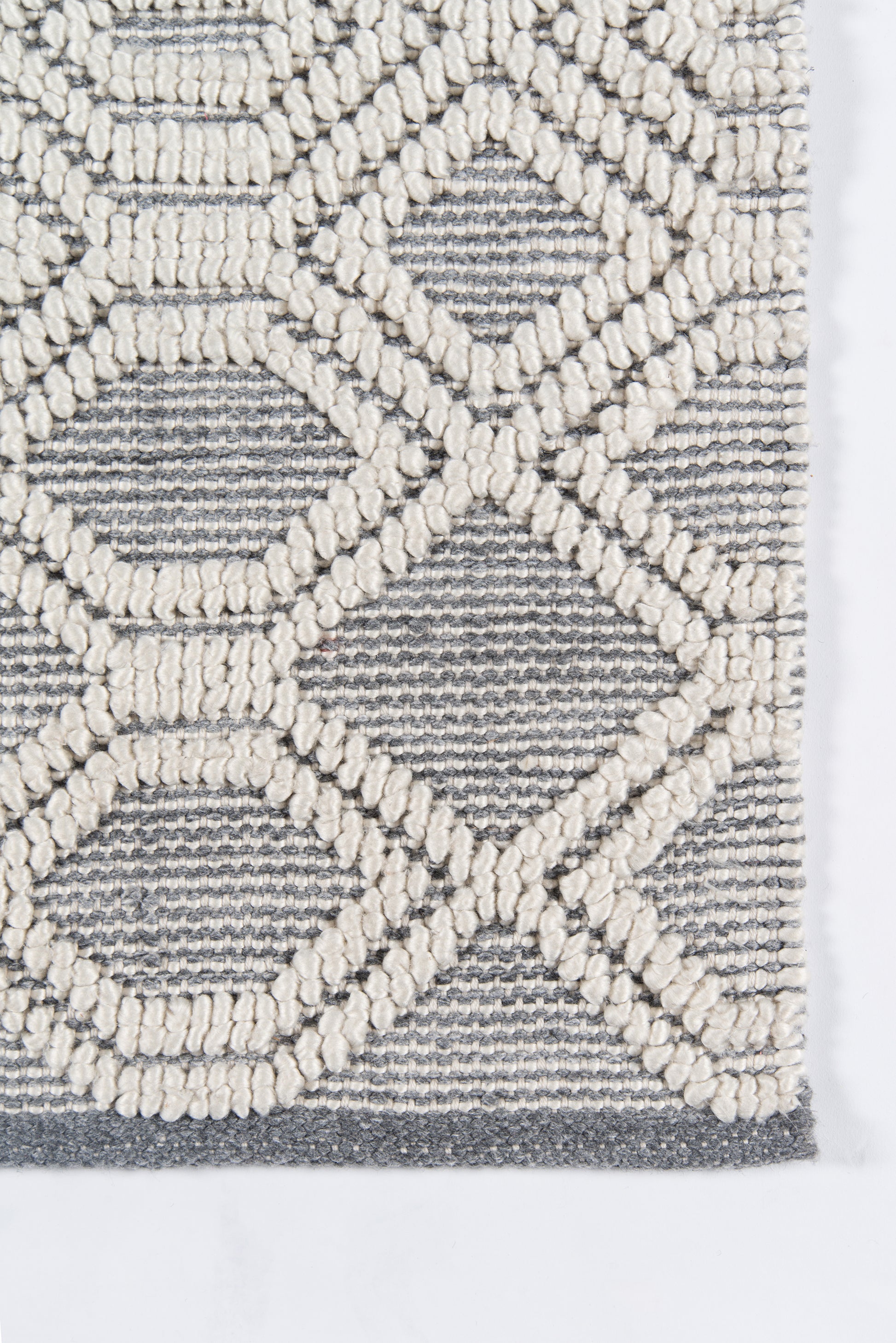 Close-up of a gray rug with cream looped geometric lattice pattern; textured tufted surface.