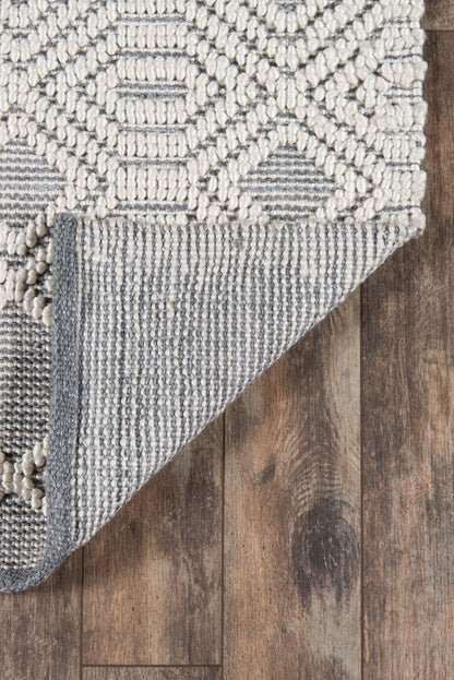 Gray & ivory textured rug with knobby loop pattern, geometric motifs, folded corner showing underside on wooden floor.