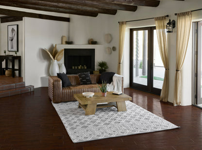 Living room with brown leather sofa, rustic wood coffee table, gray geometric rug, white fireplace, and cream curtains.