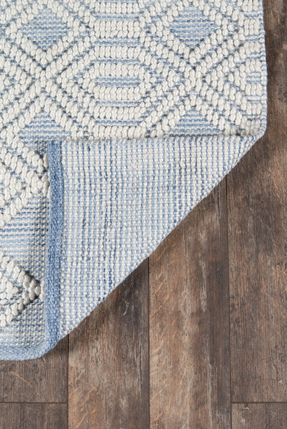 Blue & ivory geometric woven rug with diamond motifs, chunky texture, folded corner on wood floor.