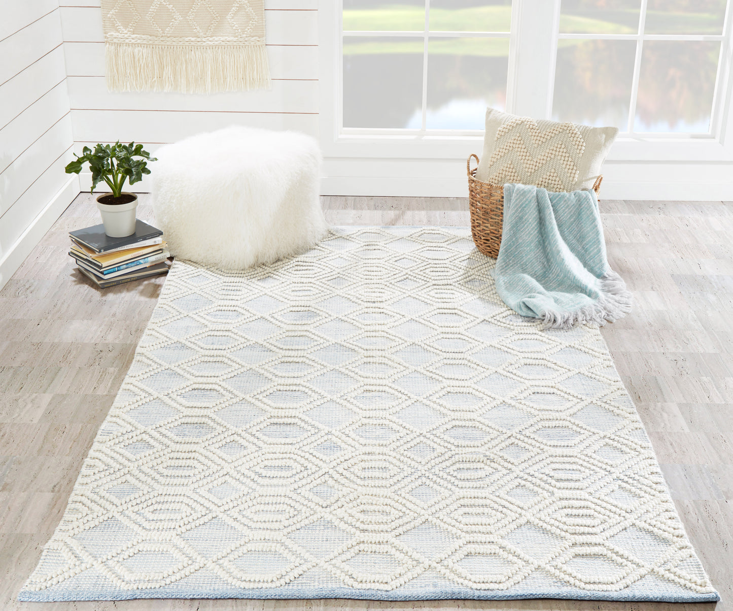 Boho woven rug in cream with pale blue geometric diamonds; cozy living room decor with pouf, basket, and throw.