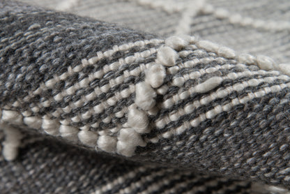 Close-up of a grey and white woven rug with boucle yarn and knotted fringe along the edge.