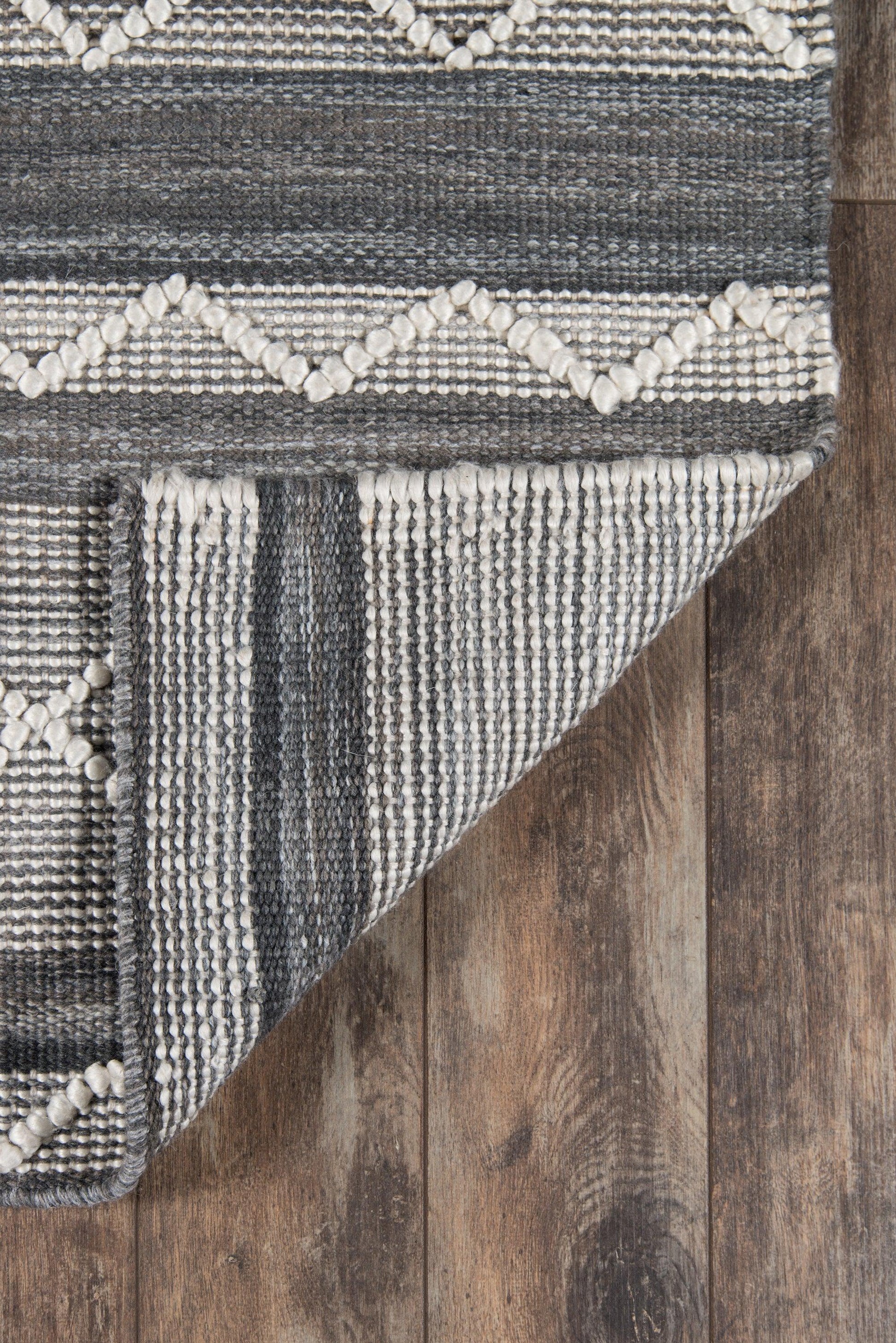 Gray and ivory geometric woven rug with diamond motifs and textured stripes, folded corner on wood floor.
