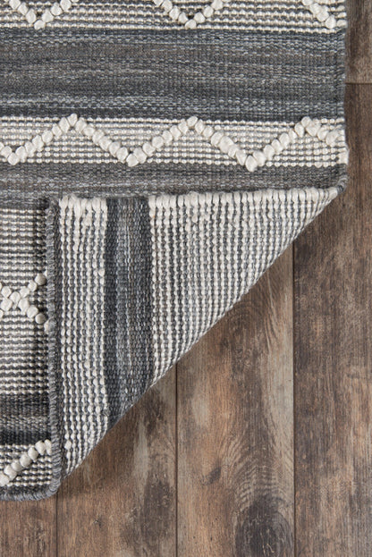 Gray and ivory geometric woven rug with diamond motifs and textured stripes, folded corner on wood floor.