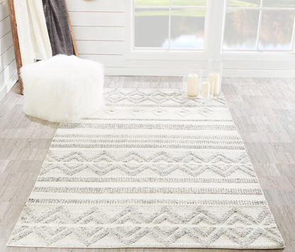 Rectangular cream-gray geometric rug with diamond and stripe patterns, fluffy white pouf, glass candle holders