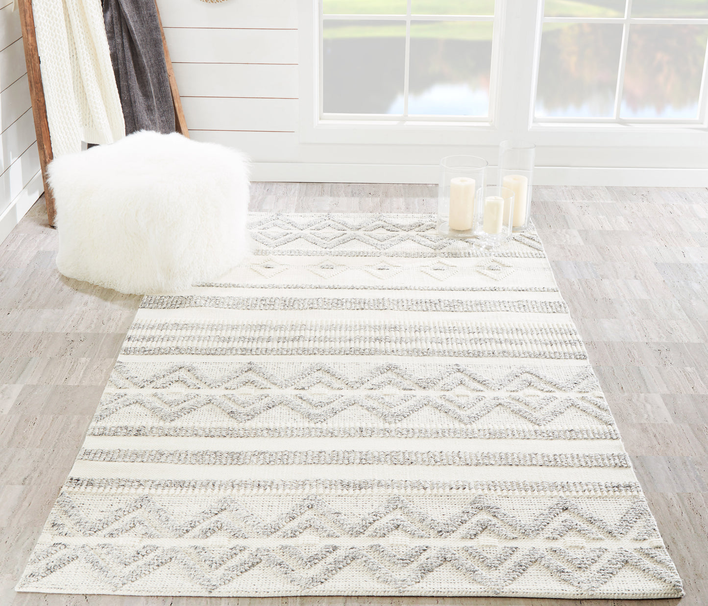 Ivory and gray geometric shag rug; boho rectangular style, with a fluffy white pouf in a bright living room.