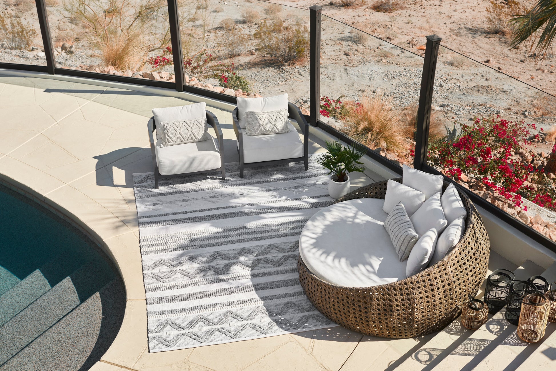 Outdoor rug, 8' x 10', beneath wicker seating with a white-cushioned daybed and gray-frame chairs beside a glass-railed pool.