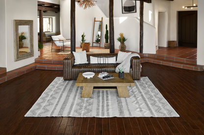 Rustic-modern living room with brown leather sofa, chunky wooden coffee table, gray patterned rug, white walls & plants.